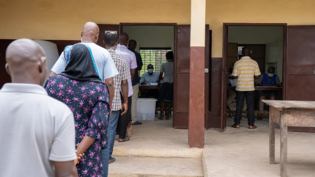 Illustration : file d'électeurs devant un bureau de vote en Guinée, avec urne et agents électoraux.
