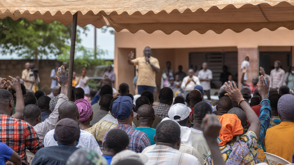 Illustration : Rassemblement politique avec citoyens écoutant un discours de campagne électorale en Afrique de l'Ouest.